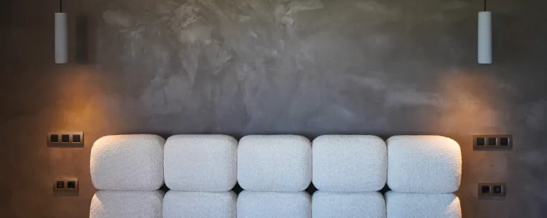 Pared de microcemento continuo en dormitorio, acabado gris cálido con cabecero tapizado